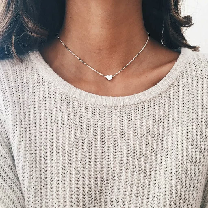 Silberne Herz-Halskette auf cremefarbenem Strickpullover, eleganter Schmuck für Damen.