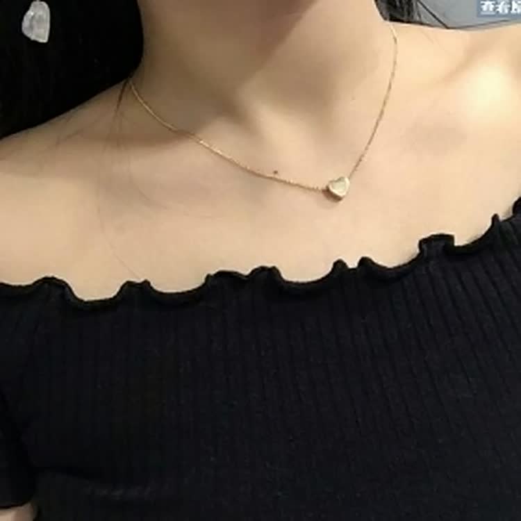 Frau mit schwarzem Oberteil trägt goldene Herz-Halskette, eleganter Schmuck, minimalistisch.