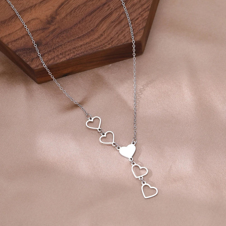 Silberne Halskette mit fünf Herzanhängern auf Holzuntergrund, eleganter Schmuck für Damen.