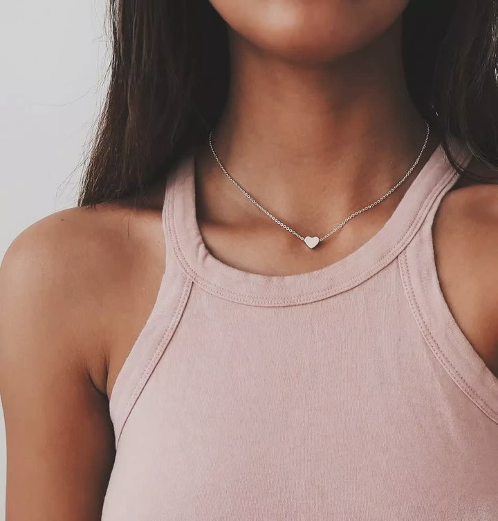 Frau trägt silberne Herz-Halskette, rosa Tanktop, minimalistisch, Schmuck für Frauen.