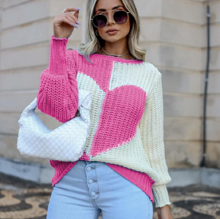 Frau in rosa-weißem Strickpullover mit Herzmotiv, blauer Jeans, weißer Tasche, Sonnenbrille.