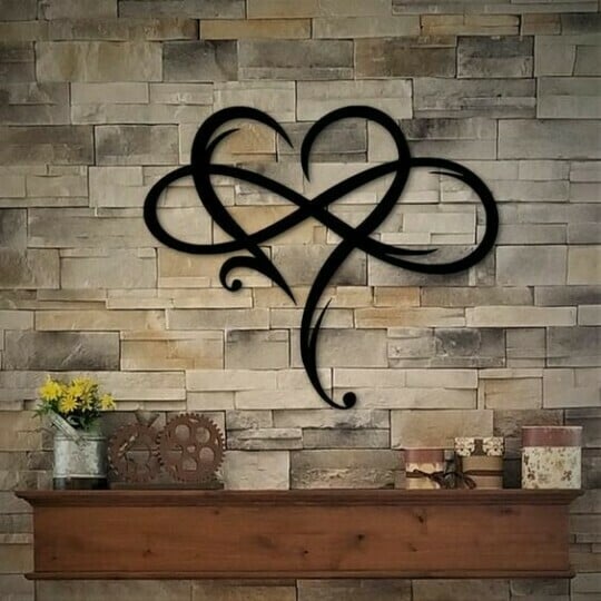 Schwarze Metall-Wanddekoration in Herzform auf Steinwand über Holzregal mit Deko-Elementen.