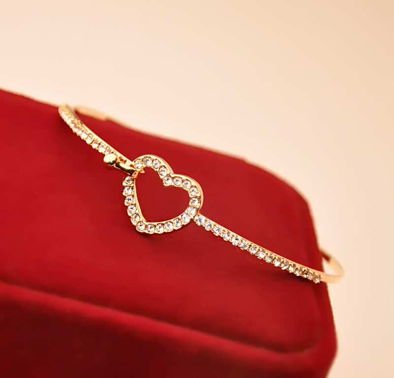 Goldenes Armband mit Herzanhänger, Strasssteinen, auf rotem Samt, eleganter Schmuck.