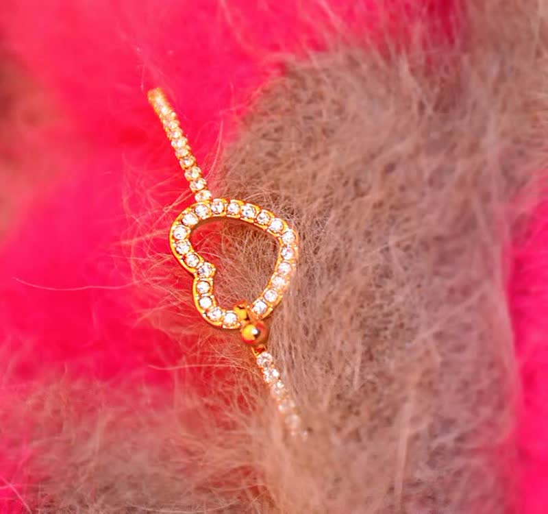 Goldenes Herzarmband mit Strasssteinen auf rosa und braunem Hintergrund, eleganter Schmuck.