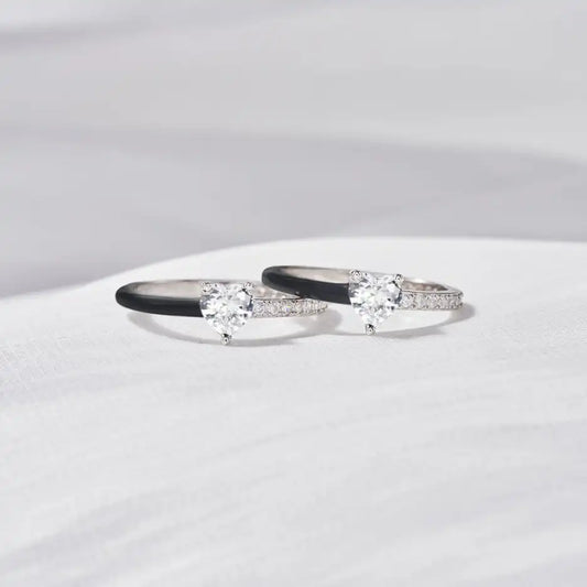 Zwei silberne Verlobungsringe mit Herz-Diamanten und schwarzen Details auf weißem Hintergrund.