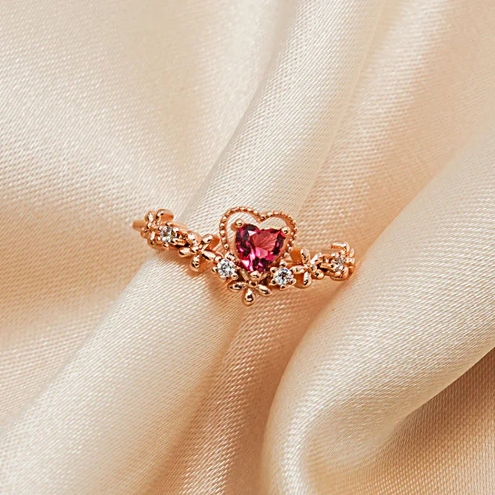 Roségoldener Ring mit herzförmigem rosa Edelstein und Diamanten auf beigem Stoff.