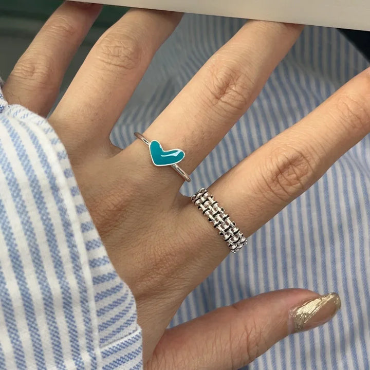 Silberring mit türkisfarbenem Herz und Kettenring auf Hand, modisches Schmuckdesign.