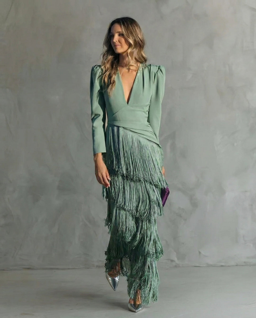 Zelené šaty s dlouhými rukávy a patrovými třásněmi na modelce v celé postavě, mírně natočené 2