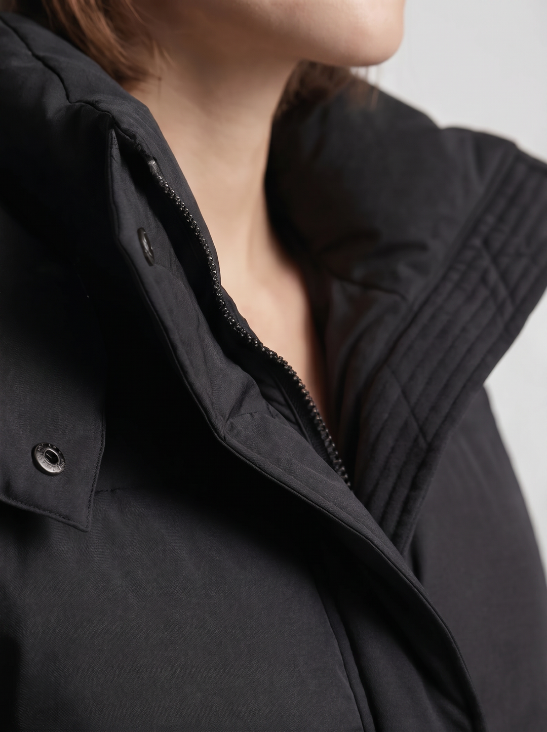 Detailní záběr na stojáček, zip a patentky černé bundy na modelce 7