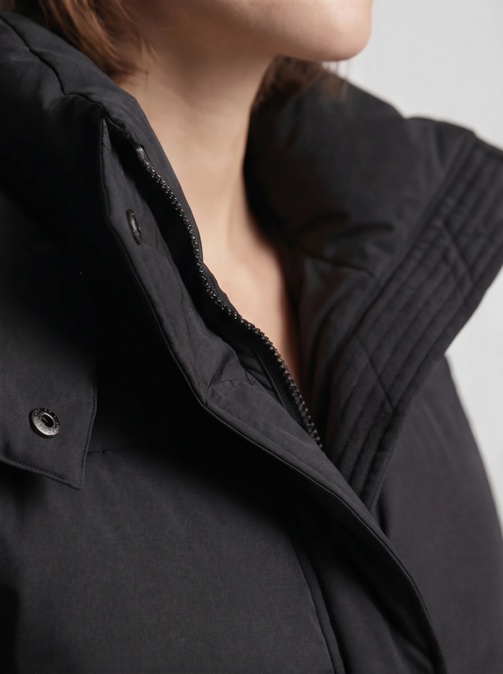 Detailní záběr na stojáček, zip a patentky černé bundy na modelce 7