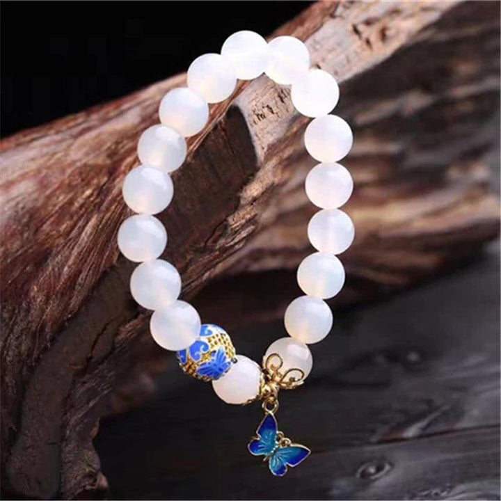 Weiße Achat-Perlenarmband mit blauem Schmetterlingsanhänger auf Holz.