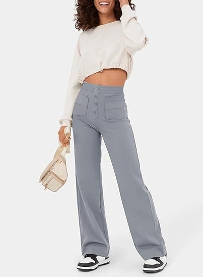 Frau in grauer, hoch taillierter, elastischer Hose und weißem Crop-Top, lächelnd mit Tasche.