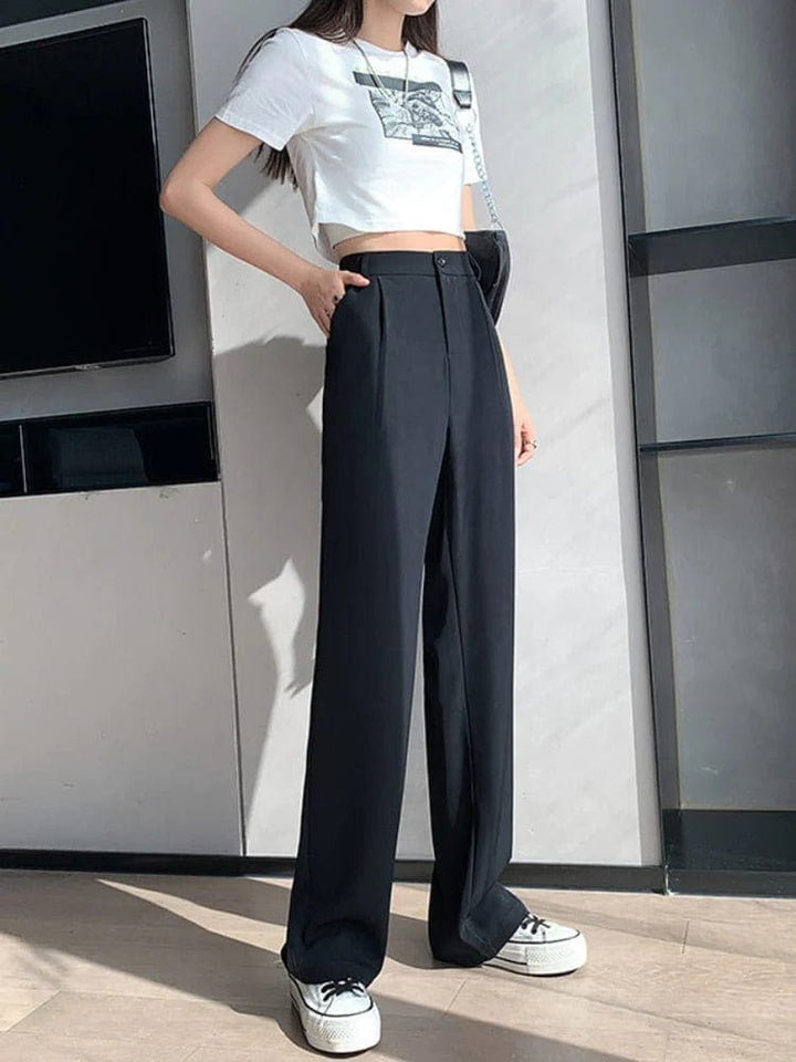 Frau trägt schwarze, hoch taillierte Hose, weißes T-Shirt, Sneakers, modisch, lässig.