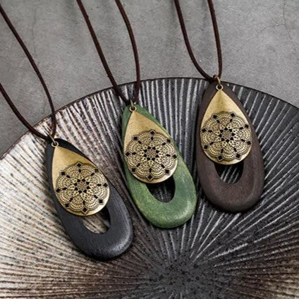 Drei handgefertigte Holzanhänger mit goldenen Mandala-Motiven auf schwarzem, grünem und braunem Holz.
