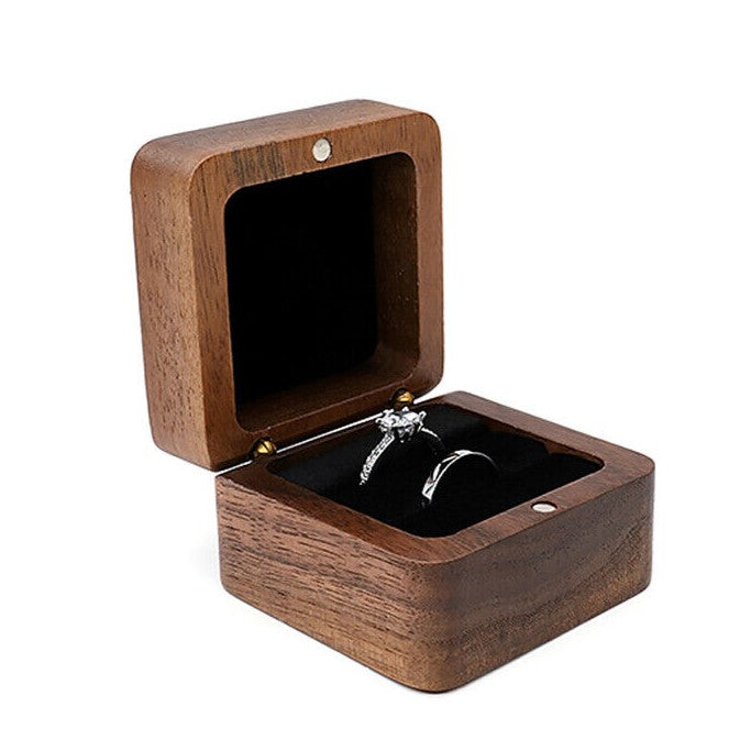 Offene Holz-Ringbox mit schwarzem Innenfutter und silbernem Verlobungsring.