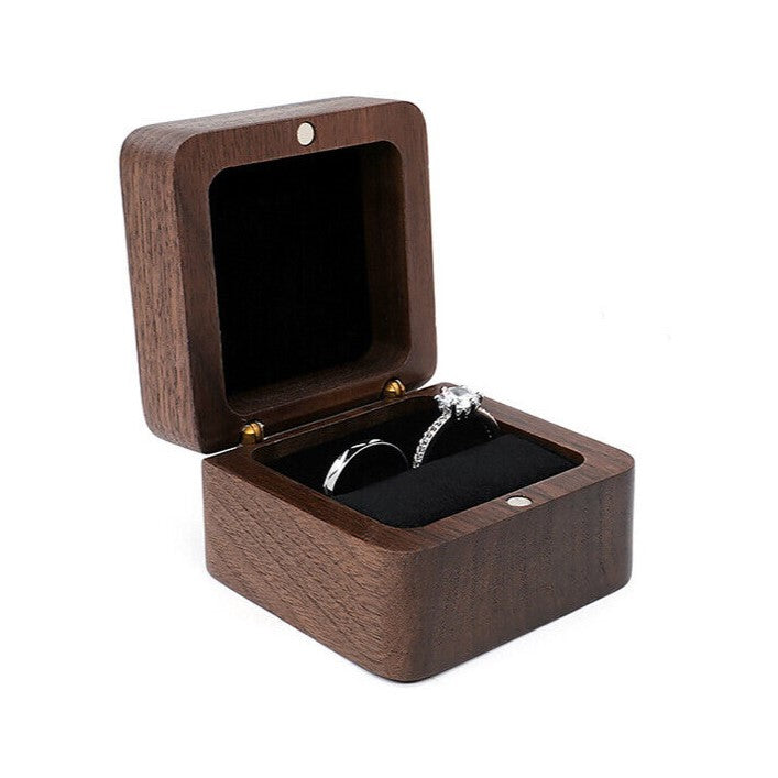 Offene Holz-Ringbox mit schwarzem Innenfutter, enthält zwei silberne Ringe.