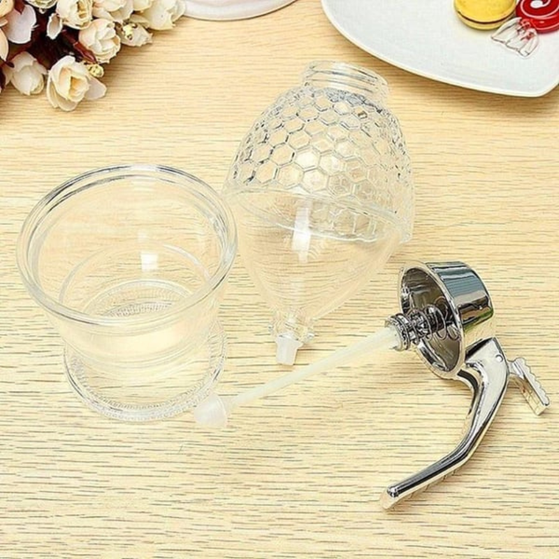 Honigspender aus Glas mit Metallgriff auf Holztisch, ideal für Küche und Frühstückstisch.