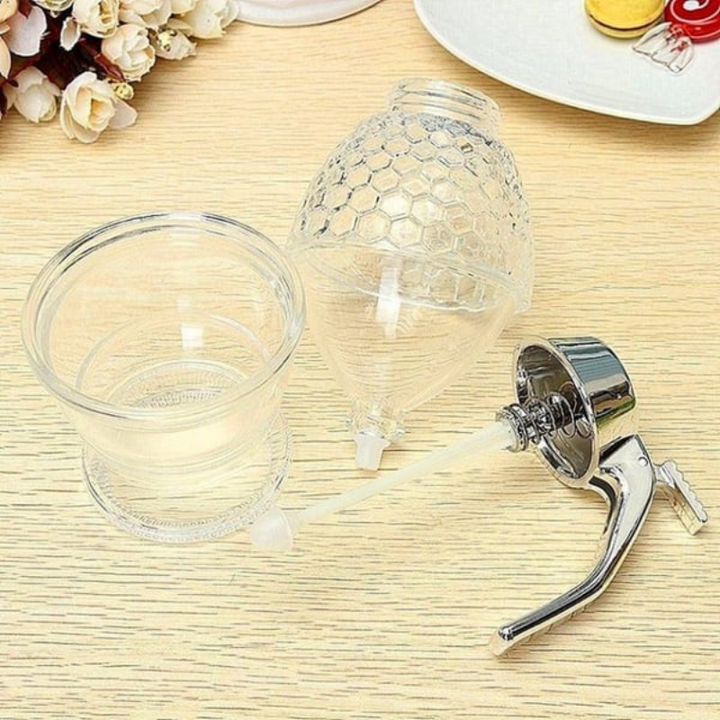 Honigspender aus Glas mit Metallgriff auf Holztisch, ideal für Küche und Frühstückstisch.