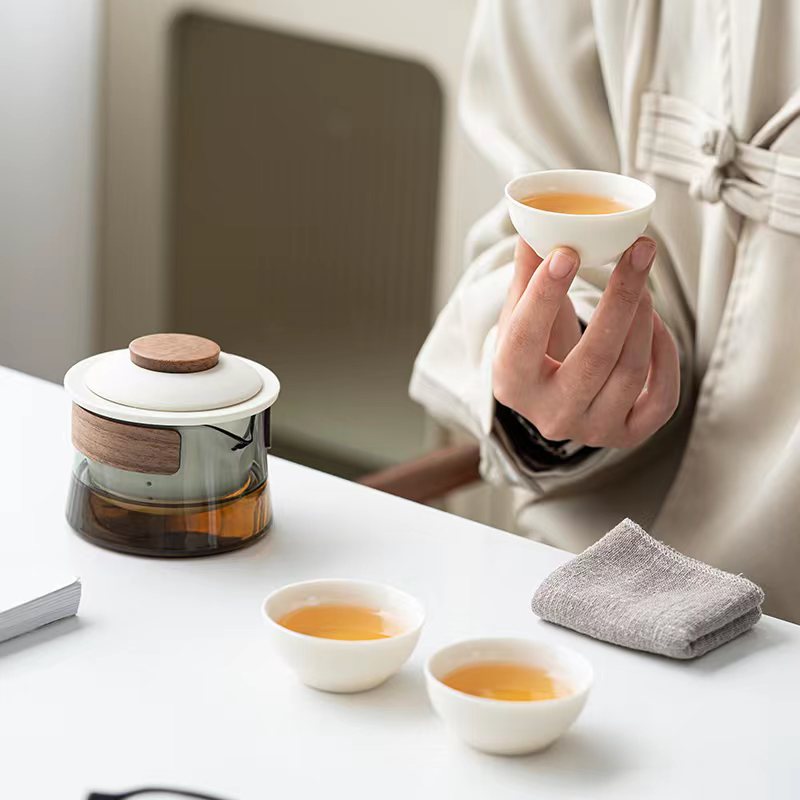 Person hält weiße Teetasse, Glasteekanne mit Holzdeckel, minimalistisch, Teeservice.
