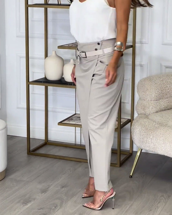 Frau in beiger Hose und weißem Top, elegante Sandalen, modernes Wohnzimmer, stilvolle Dekoration.