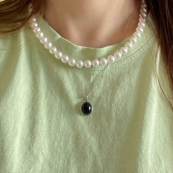 Frau mit Perlenkette und schwarzem Anhänger auf grünem T-Shirt, eleganter Schmuck, Modeaccessoire.