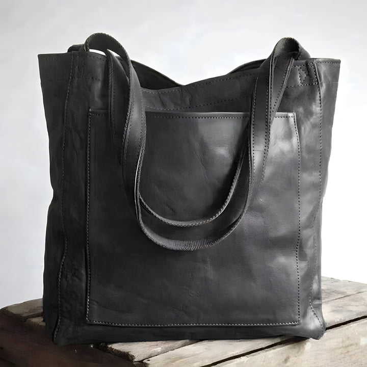 Schwarze Ledertasche mit Tragegriffen auf Holztisch, modisch und geräumig.