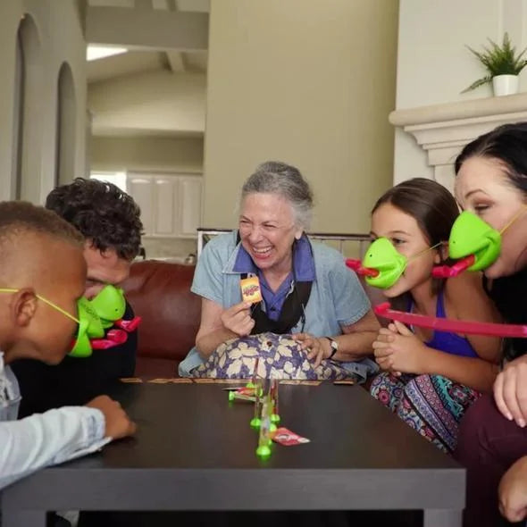 Personen spielen mit grünen Froschmasken am Tisch, lachen, Brettspiel, Wohnzimmer, Freizeit.