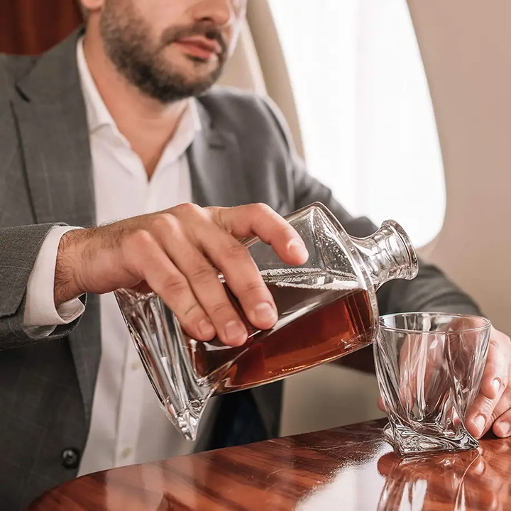 Mann im Anzug gießt Whisky aus Kristallkaraffe in Glas auf Flugzeugtisch.