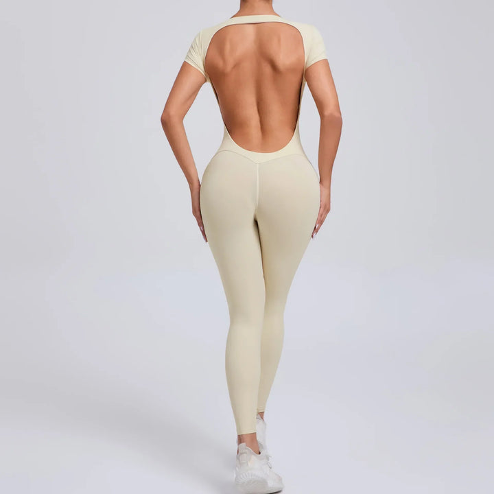 Frau in beigefarbenem, rückenfreiem Jumpsuit, Sportbekleidung, Ganzkörperansicht.
