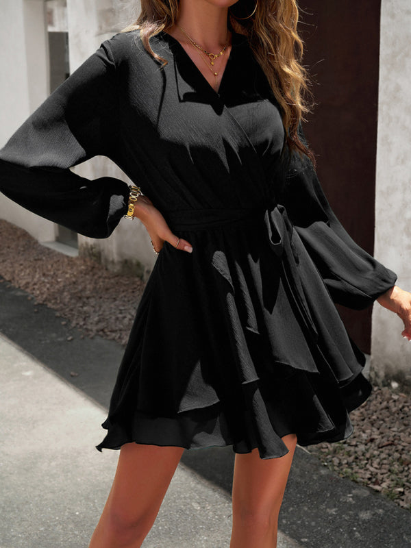 Frau in schwarzem Wickelkleid mit langen Ärmeln, elegantes Design, draußen stehend.