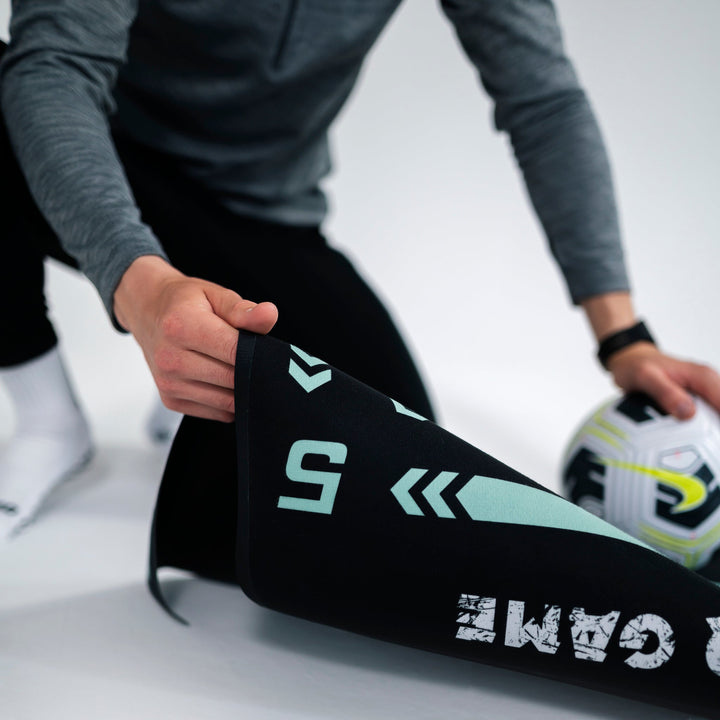 Person rollt schwarzen Fitnessmatte mit Fußballmotiv aus, Sportbekleidung, Indoor-Training.