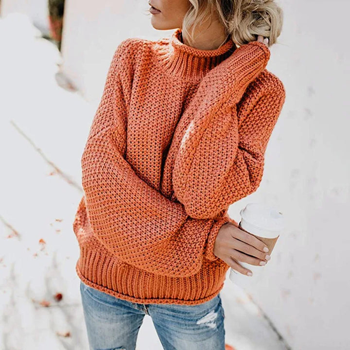 Frau in orangefarbenem Strickpullover hält Kaffeebecher, lässige Herbstmode, Jeans.