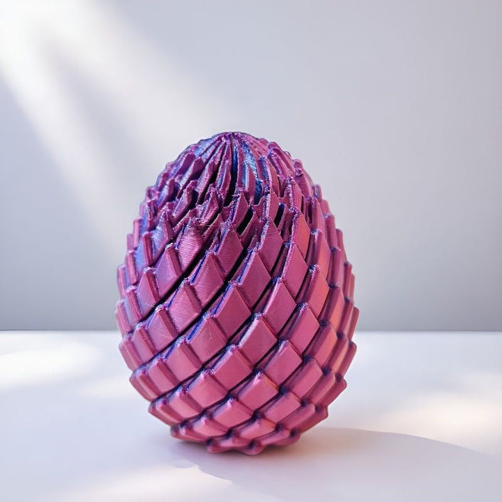 Purpurově růžové vejce s kloubovými šupinami stojí na bílém povrchu ve světle ze strany. 10