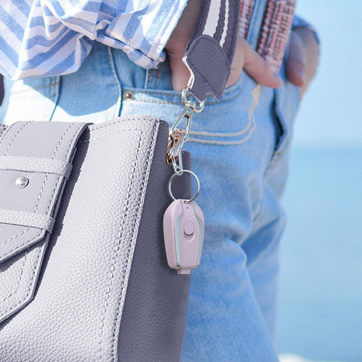 Grauer Ledertasche mit rosa Schlüsselanhänger, Jeans, blauem Hemd, am Meer.