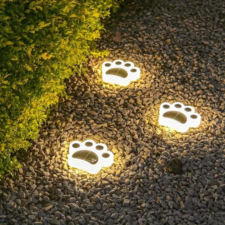 Leuchtende Pfotenabdruck-Solarleuchten auf Kiesweg neben grüner Hecke im Garten.