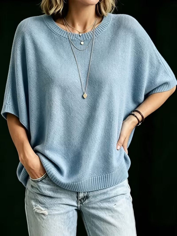 Světle modrý volný pletený top na modelce s rukou v bok a druhou v kapse džínů. 15