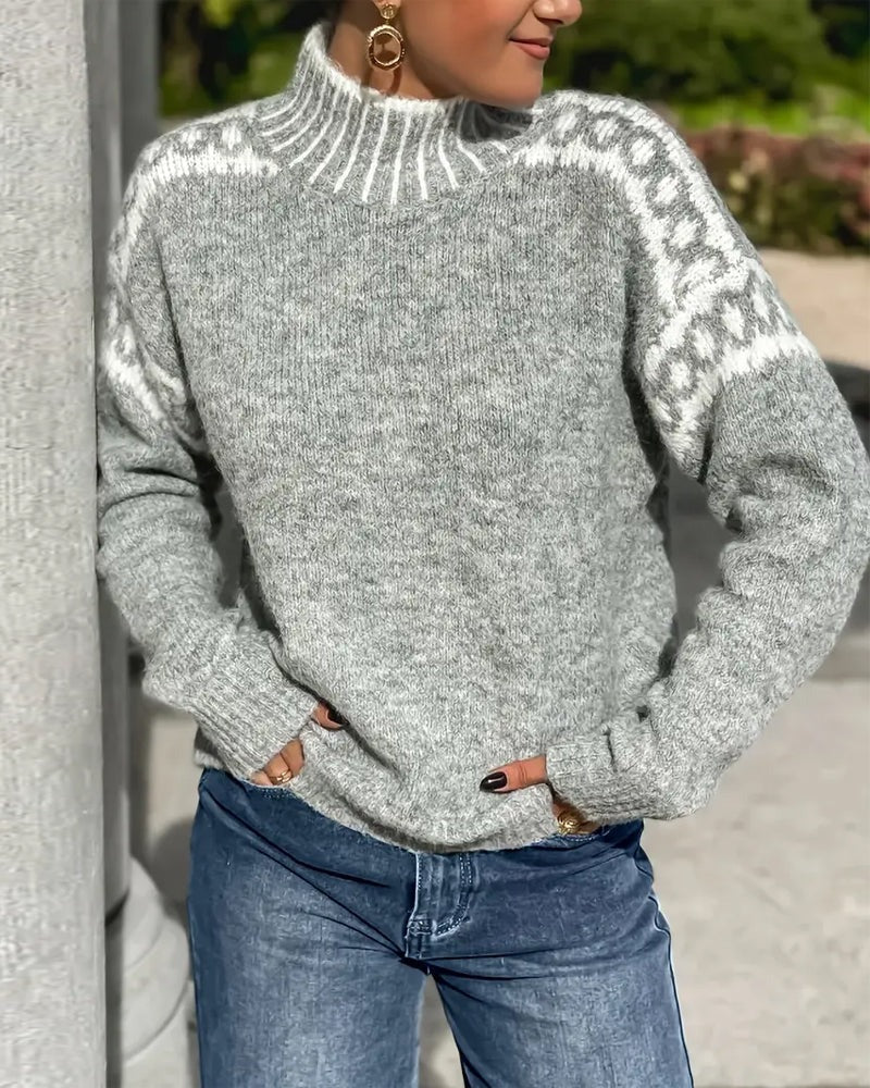 Šedý pletený svetr se stojáčkem a bílým ozdobným vzorem na ramenou, modelka v džínách u sloupu. 5