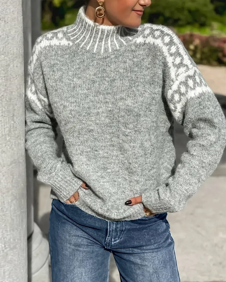 Šedý pletený svetr se stojáčkem a bílým ozdobným vzorem na ramenou, modelka v džínách u sloupu. 5