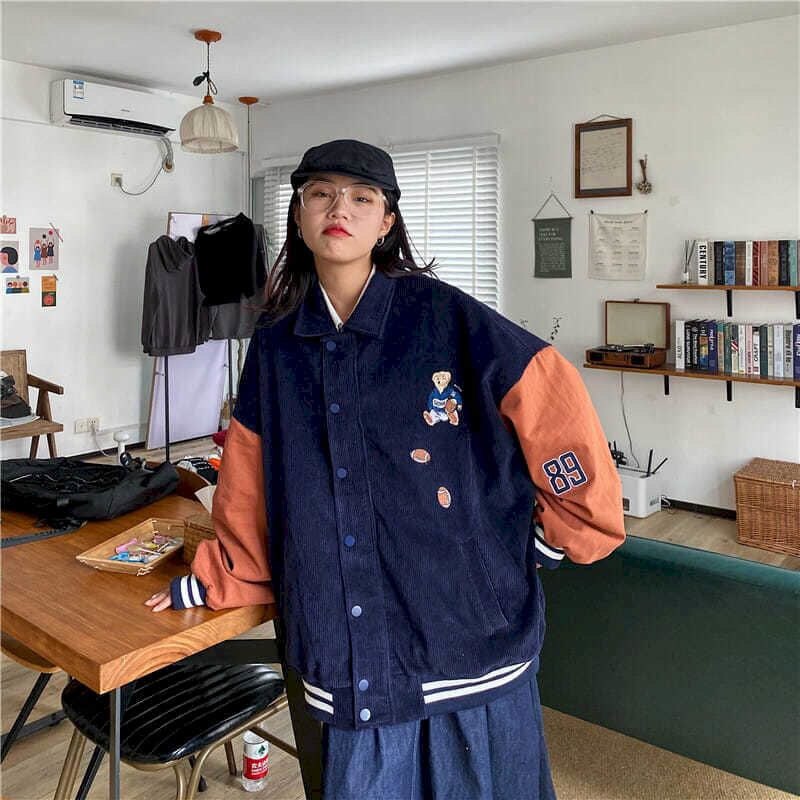Frau trägt dunkelblaue Collegejacke mit orangenen Ärmeln und Stickerei, modisch, lässig.