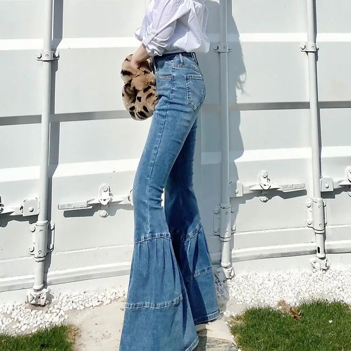 Frau in blauen Schlagjeans, weißer Bluse, hält Leopardenmuster-Tasche, draußen stehend.