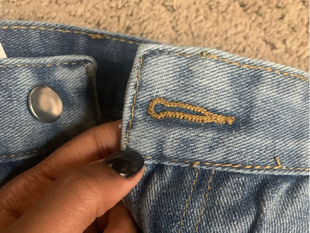 Damenjeans aus blauem Denim mit goldener Stickerei und silbernem Knopf, Nahaufnahme.