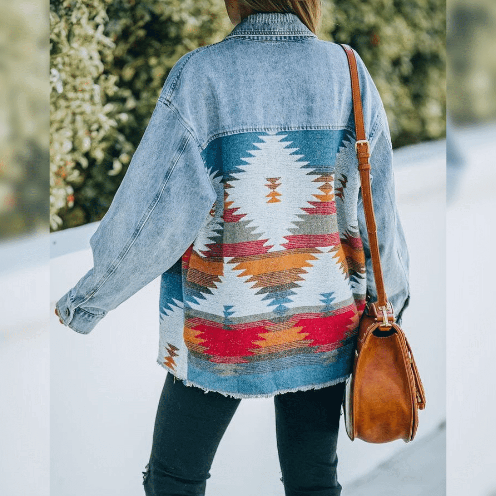 Frau in blauer Jeansjacke mit buntem Aztekenmuster und brauner Ledertasche von hinten.