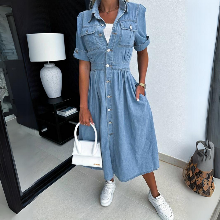 Frau in blauem Jeanskleid mit weißen Sneakers und weißer Handtasche in modernem Raum.