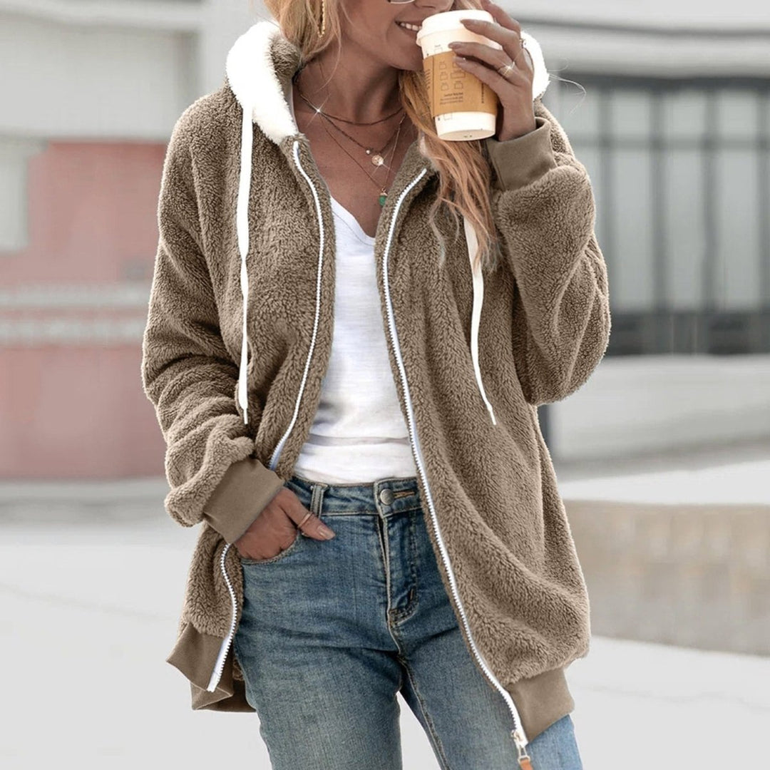 Frau in brauner Teddyweste mit Reißverschluss, Kapuze, hält Kaffeebecher, lässige Mode.