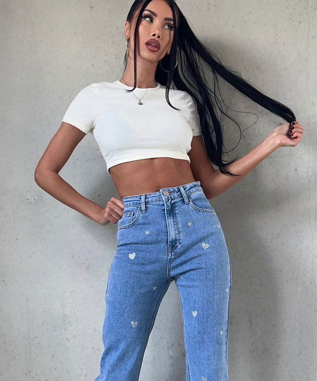 Frau in weißem Crop-Top und blauer Jeans mit Herzmuster, modisch, lässig, trendige Damenmode.