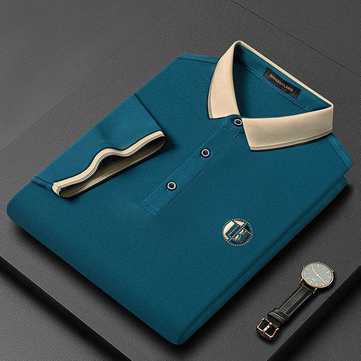 Dunkelgrünes Herren-Poloshirt mit beigem Kragen, Knöpfen und Uhr auf grauem Hintergrund.