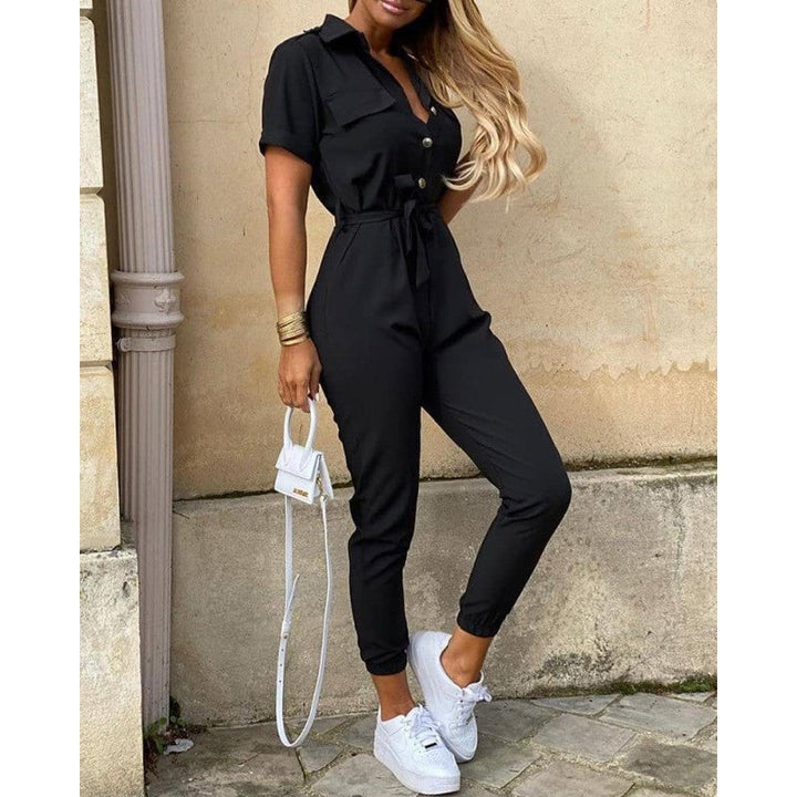 Frau in schwarzem Jumpsuit mit Gürtel, kurzen Ärmeln, weißen Sneakers, modisch, elegant.