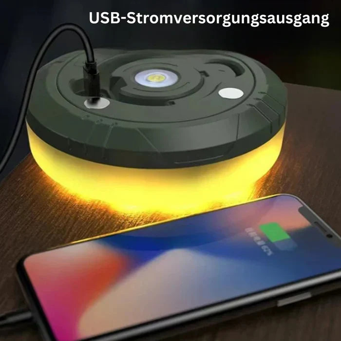 Tragbare LED-Lampe mit USB-Ladefunktion, leuchtend gelb, auf Holztisch neben Smartphone.