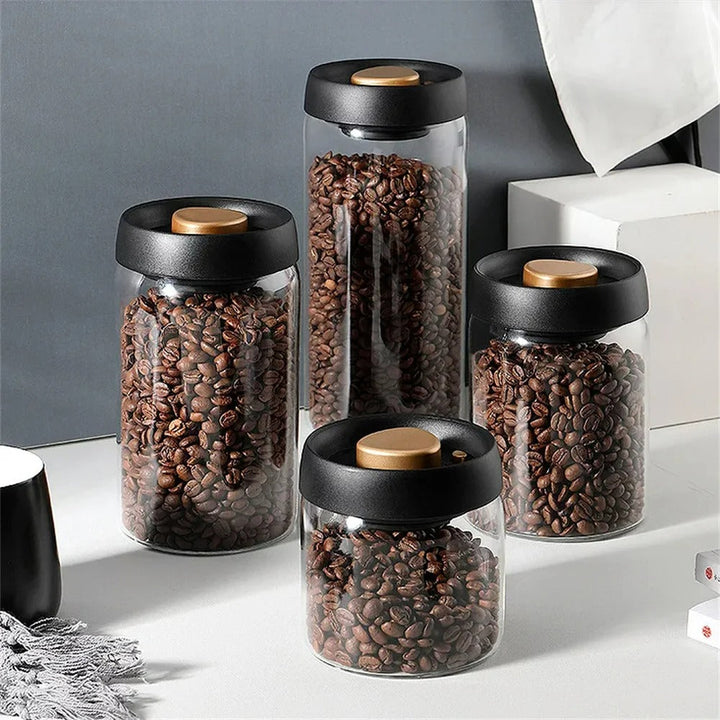 Vier Glasbehälter mit schwarzen Deckeln, gefüllt mit Kaffeebohnen, auf grauem Hintergrund.