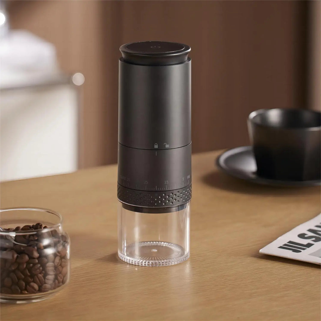 Schwarze Kaffeemühle aus Edelstahl auf Holztisch neben Kaffeebohnen und Tasse.